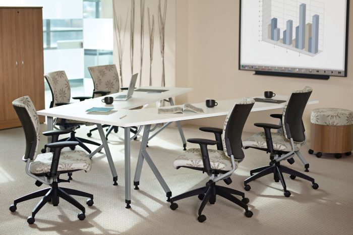 Small conference room featuring five patterned Graphic chairs placed at a V-shaped conference table. A bar graph is projected on the screen in front.
