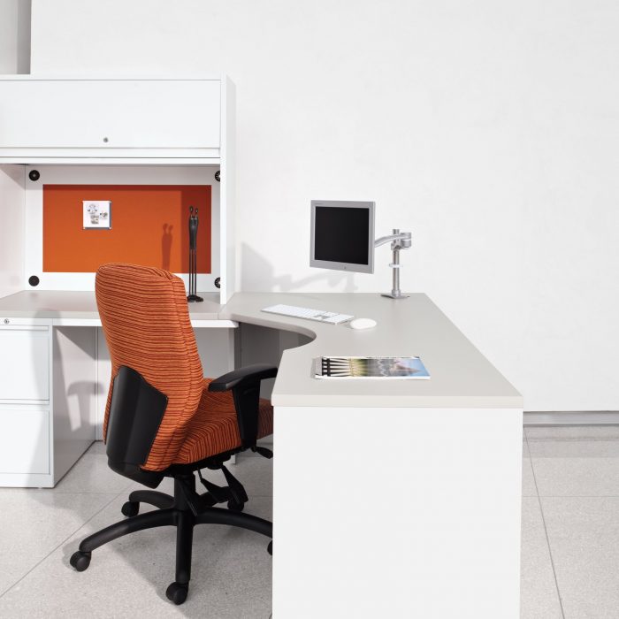 Closeup of a Synopsis chair placed within a corner L-shaped desk. It has a medium height back, and uses orange striped pattern on the cushion.