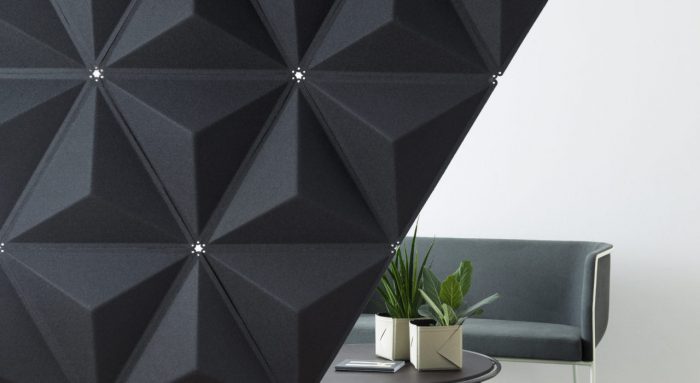 Studio shot of a Aircone wall partition, set up in a white studio. The partition has a diagonal area that shows a couch and coffee table behind.