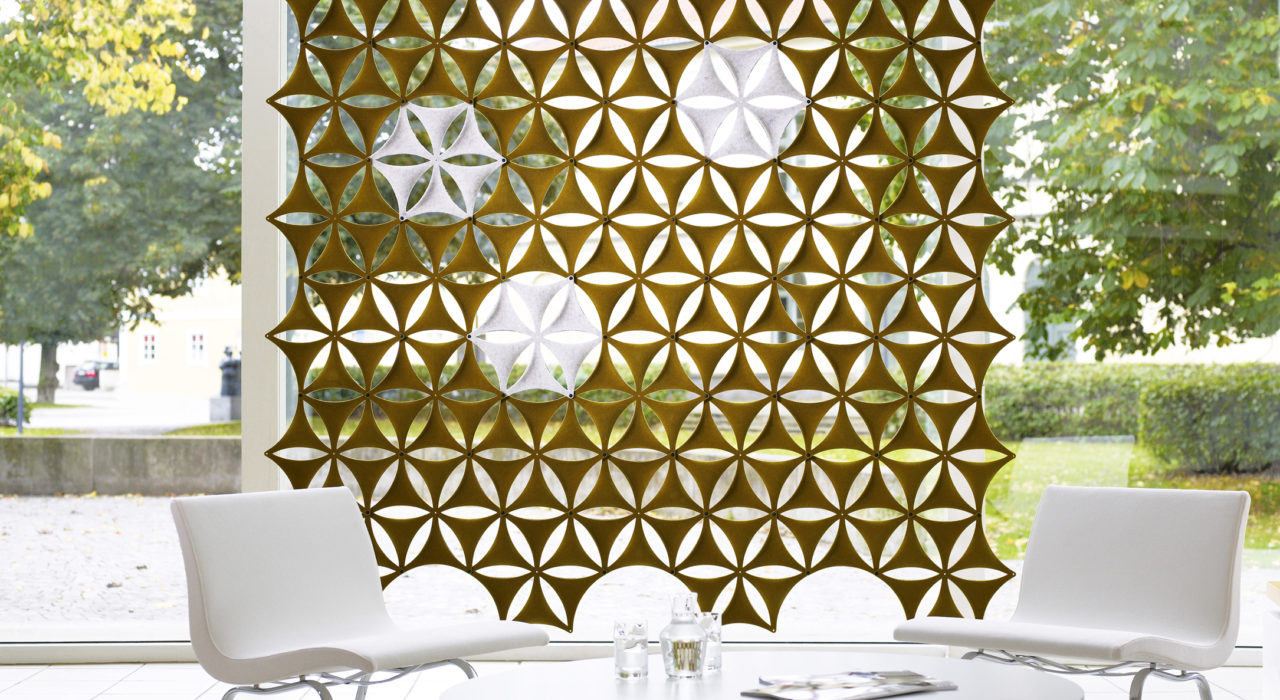 Studio shot of olive colored Airflake acoustics hung along the outer wall of the lobby. Two white chairs are placed across a glass table from one another.