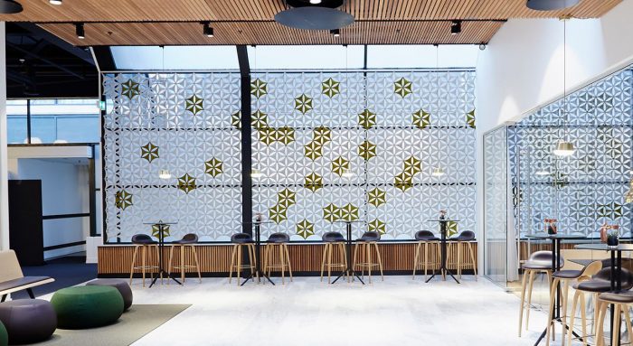 Studio shot of Airflake acoustics set up in a large lounge area. Tall cocktail tables and barstools are placed along the back wall. Airflake acoustics are placed along the wall, backlit in white.