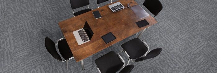 Studio shot from above a wooden table, with six chairs placed around. This area is dressed in Outfitter model carpeting.