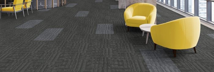 Studio shot of the front guest area, using Outfitter carpeting. Two yellow cushioned chairs surround a small round coffee table.