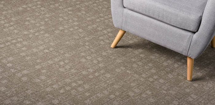 Studio shot of a wooden legged easy chair resting on Oxford carpeting.