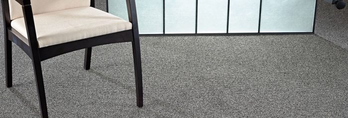 Studio shot of a Structure carpeting. A chair with a wooden frame is placed in front of a lit screen.