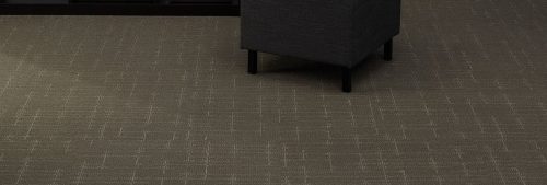 Studio shot of a cushioned ottoman resting on top of Tempo carpeting.