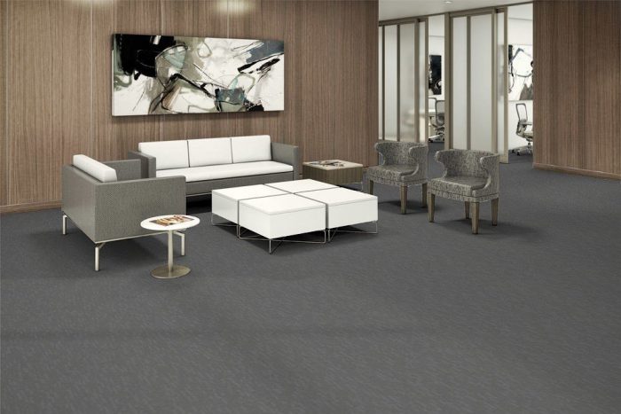 Tone model flooring in a large lounge area. A wide abstract painting hangs over a long couch. A paneled coffee table is placed in front, with mid-backed chairs on each side.