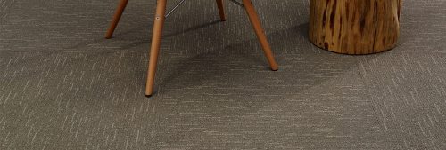Studio photography of Tone carpeting, with a wooden end table and chair placed on top. Each square has been given a quarter turn for the design.