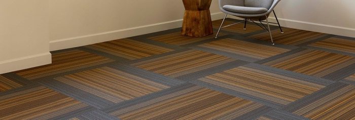 Studio shot of Umbra II carpeting, with each square given a quarter turn. In the corner is a stylish wooden end table, with a scooped guest chair just beside.