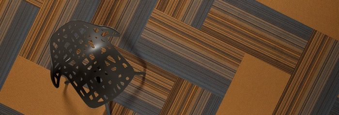 Studio shot of a dark grey plastic chair, resting on Umbra II carpeting. The carpet squares are arranged in a herringbone design. The chair's seat and back has been given a stylish cutout aesthetic.