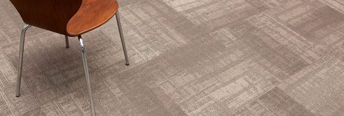 Studio shot of a metal framed chair placed on Well Versed model carpet. The wooden seat and back of the chair adds contrast to the subtle sand colored gradient of the floor.