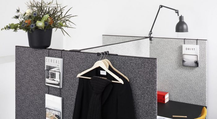 Studio shot of dB privacy screening on a pair of cubicles. Small wire racks hang pamphlets on the outside, next to a business suit hung over the partition.