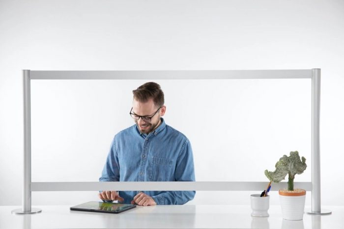 A man stands behind a counter, looking at his tablet. A Counter Shield Wrap model screen separates him from the space in front.